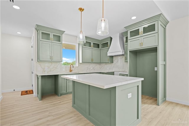 kitchen featuring light stone countertops, custom range hood, sink, green cabinetry, and a kitchen island