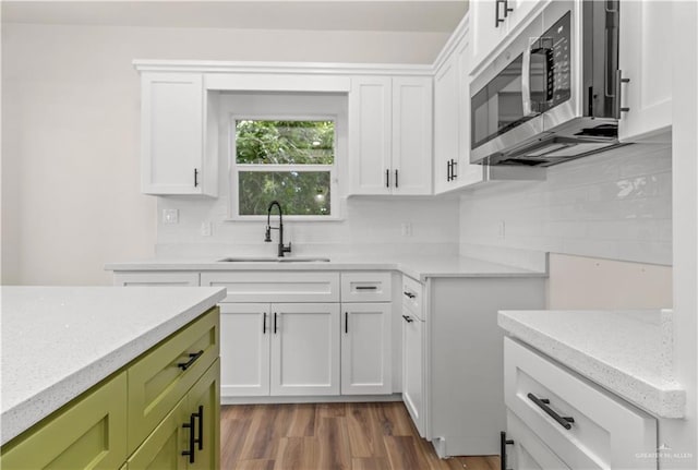 kitchen with decorative backsplash, light wood-type flooring, sink, green cabinetry, and white cabinetry