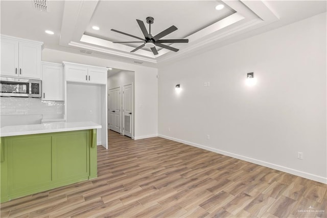 kitchen featuring backsplash, a tray ceiling, ceiling fan, light hardwood / wood-style flooring, and white cabinets