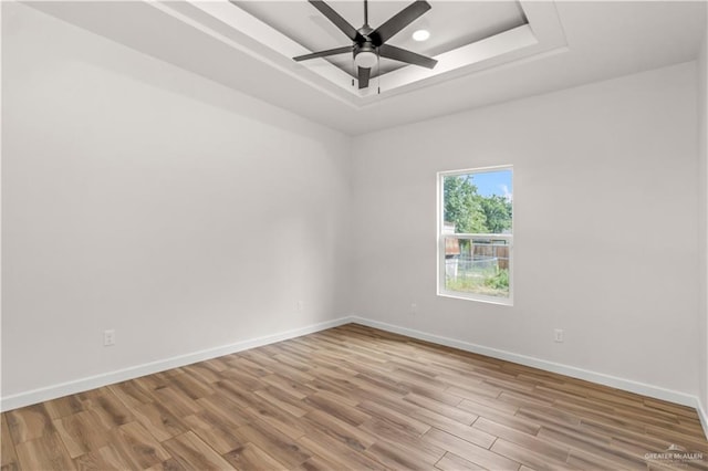 empty room with ceiling fan, a raised ceiling, and light wood-type flooring