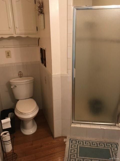 bathroom featuring hardwood / wood-style floors, toilet, tile walls, and a shower with shower door