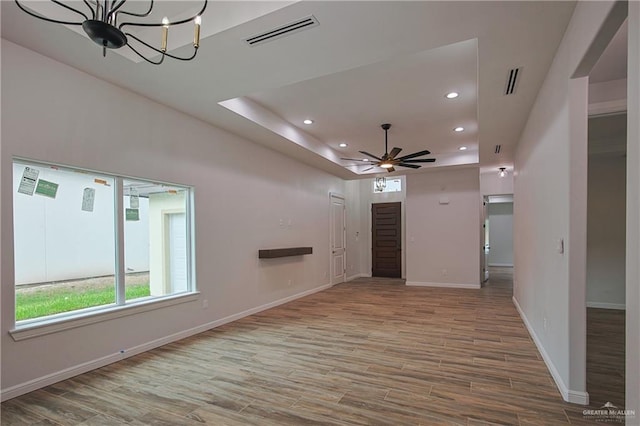 unfurnished living room with ceiling fan with notable chandelier and a raised ceiling