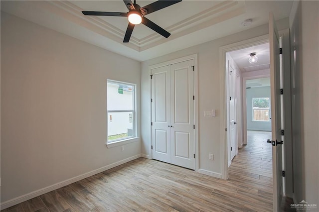 unfurnished bedroom with ceiling fan, a raised ceiling, light hardwood / wood-style flooring, a closet, and ornamental molding