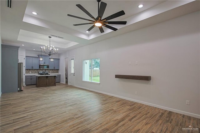 unfurnished living room featuring a tray ceiling, wood-type flooring, and ceiling fan with notable chandelier