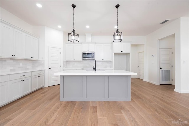 kitchen with white cabinetry, decorative light fixtures, decorative backsplash, a center island with sink, and light wood-type flooring