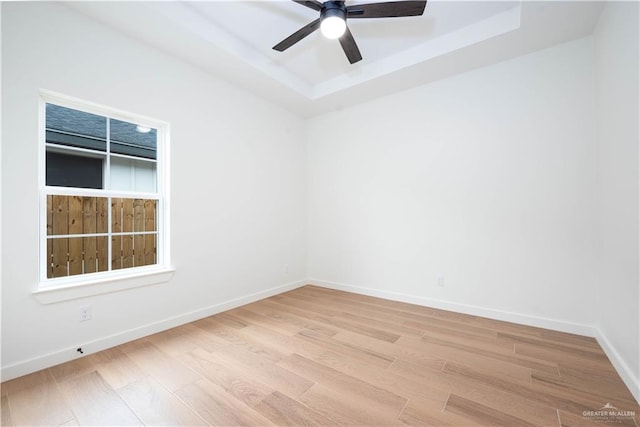 spare room with light wood-type flooring, a tray ceiling, and ceiling fan