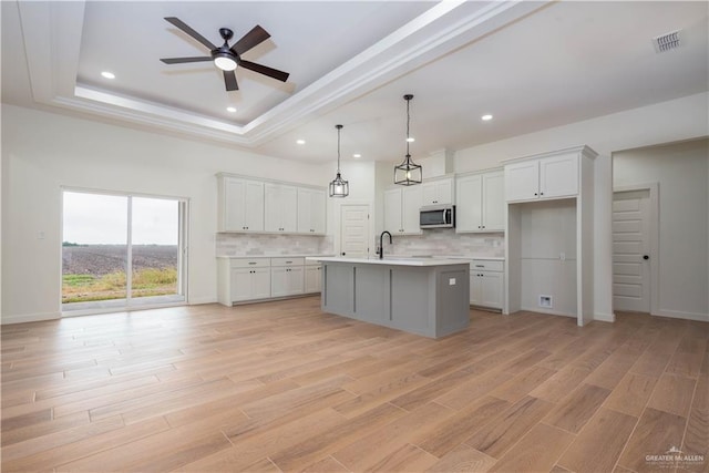 kitchen with white cabinetry, hanging light fixtures, a kitchen island with sink, and light wood-type flooring