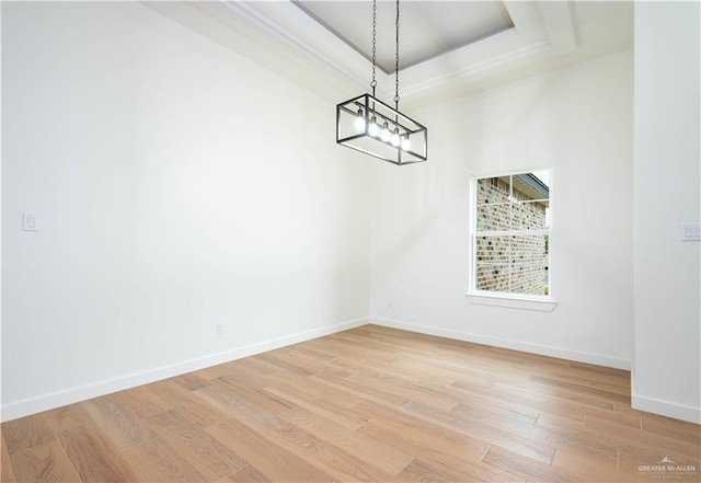 unfurnished dining area with light hardwood / wood-style floors, a tray ceiling, and a notable chandelier