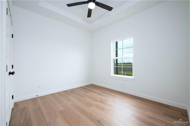 unfurnished room featuring ceiling fan, light wood-type flooring, and a tray ceiling