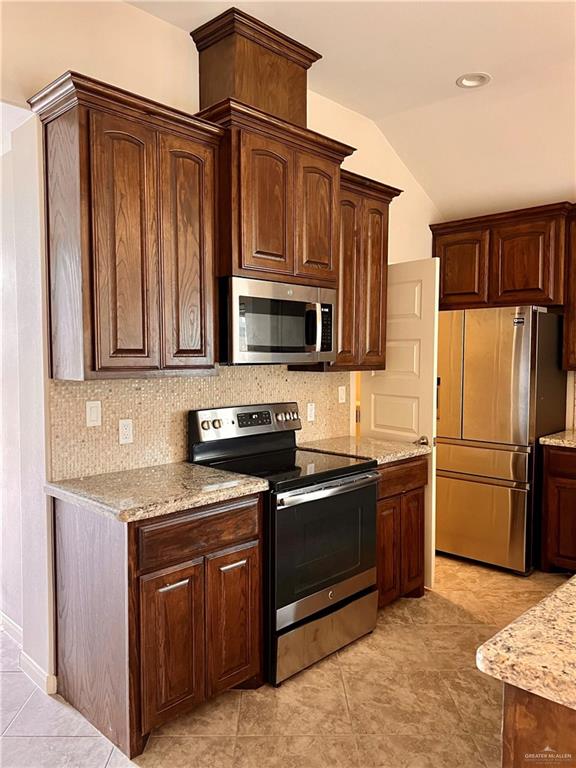 kitchen featuring lofted ceiling, decorative backsplash, light stone countertops, appliances with stainless steel finishes, and light tile patterned flooring