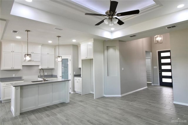 kitchen with a kitchen island with sink, white cabinetry, sink, and hanging light fixtures