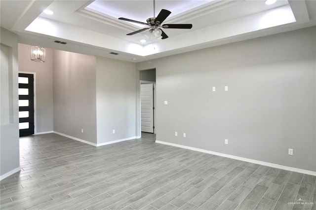 unfurnished room with ceiling fan with notable chandelier and a raised ceiling