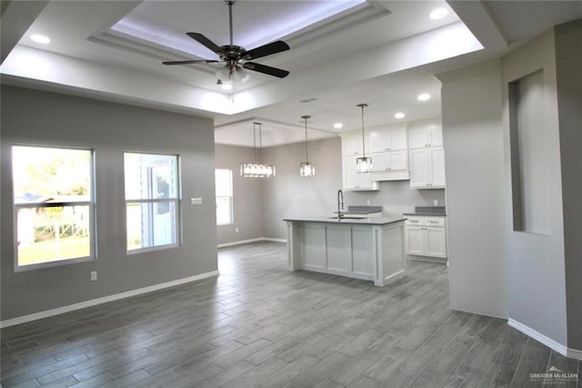 kitchen with ceiling fan with notable chandelier, a tray ceiling, a center island with sink, white cabinetry, and hanging light fixtures