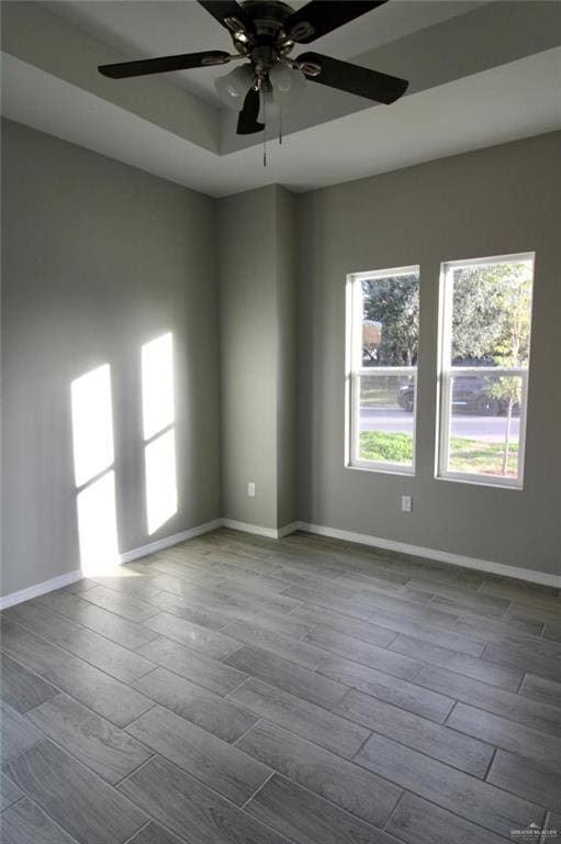 empty room with light wood-type flooring, a raised ceiling, and ceiling fan