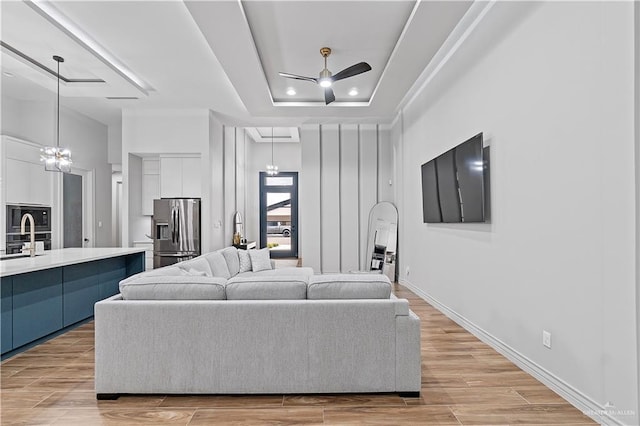 living room with ceiling fan with notable chandelier, light hardwood / wood-style floors, a tray ceiling, and sink