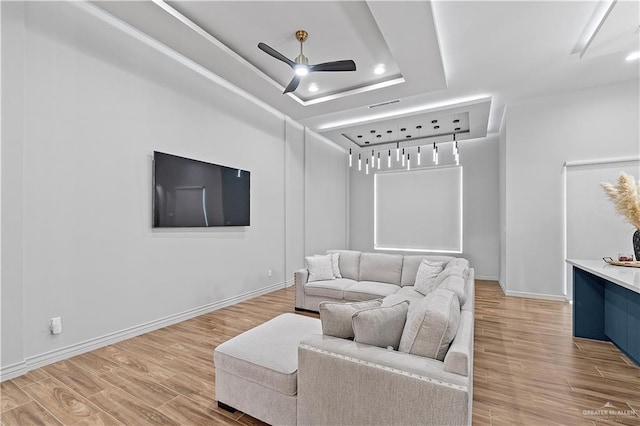 living room featuring wood-type flooring, a tray ceiling, and ceiling fan