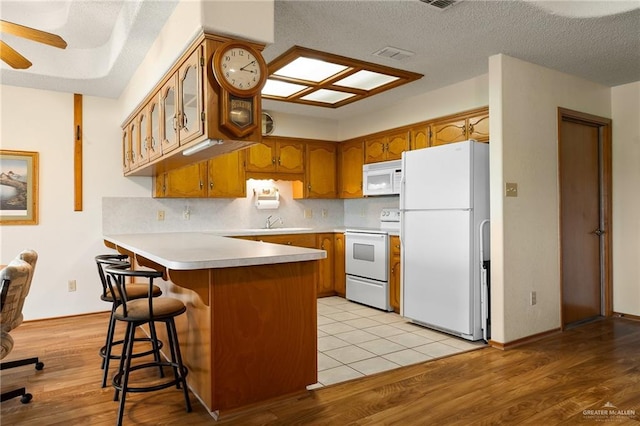 kitchen with white appliances, light hardwood / wood-style flooring, a textured ceiling, kitchen peninsula, and a breakfast bar area