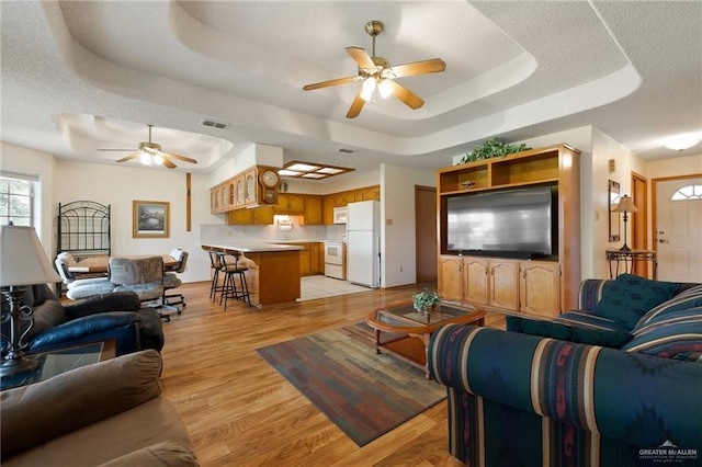 living room featuring ceiling fan, light wood-type flooring, a textured ceiling, and a tray ceiling