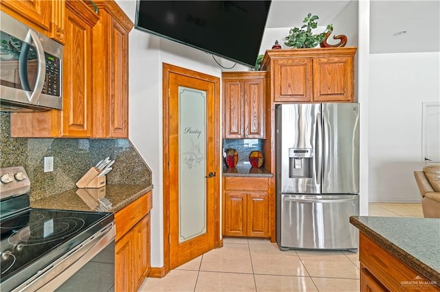 kitchen featuring stainless steel appliances, brown cabinets, backsplash, and light tile patterned floors