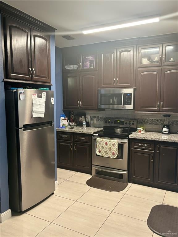 kitchen with light stone countertops, appliances with stainless steel finishes, backsplash, dark brown cabinetry, and light tile patterned flooring