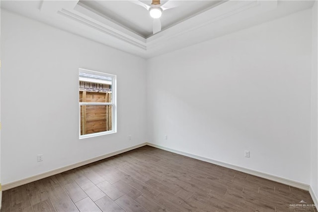 empty room featuring a ceiling fan, a raised ceiling, baseboards, and wood finished floors