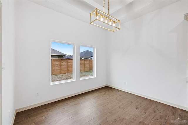 unfurnished room featuring a notable chandelier, baseboards, and wood finished floors