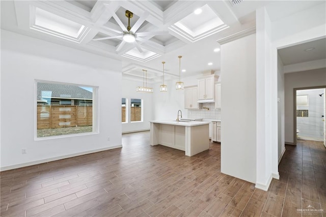 kitchen with backsplash, dark wood-type flooring, a kitchen island with sink, light countertops, and a sink