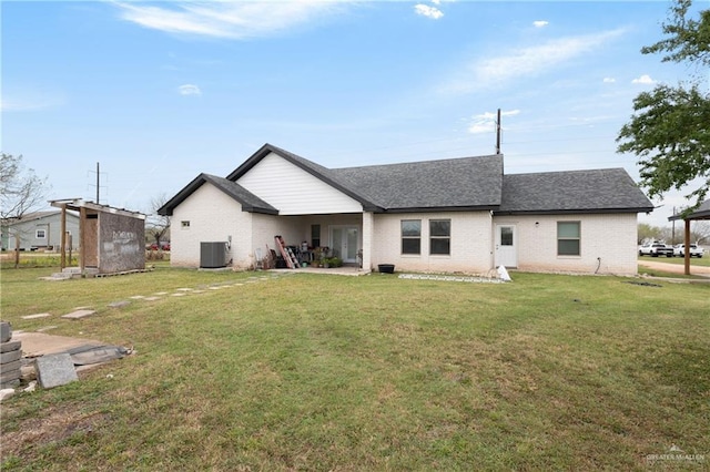 rear view of property with a yard, central AC unit, a shingled roof, and brick siding