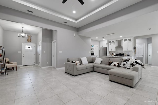 living room with light tile patterned floors, a tray ceiling, visible vents, and baseboards