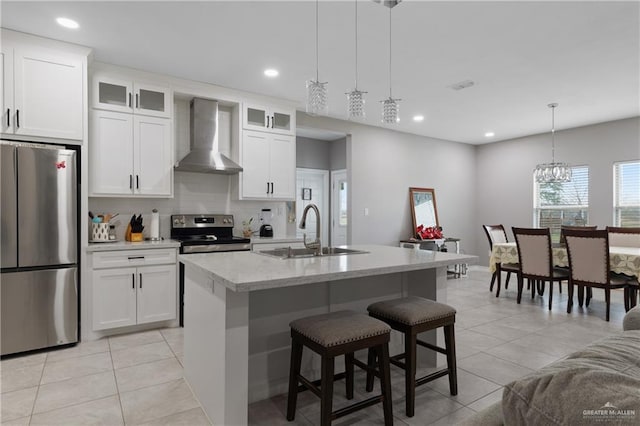 kitchen featuring light tile patterned floors, a center island with sink, stainless steel appliances, wall chimney range hood, and a sink