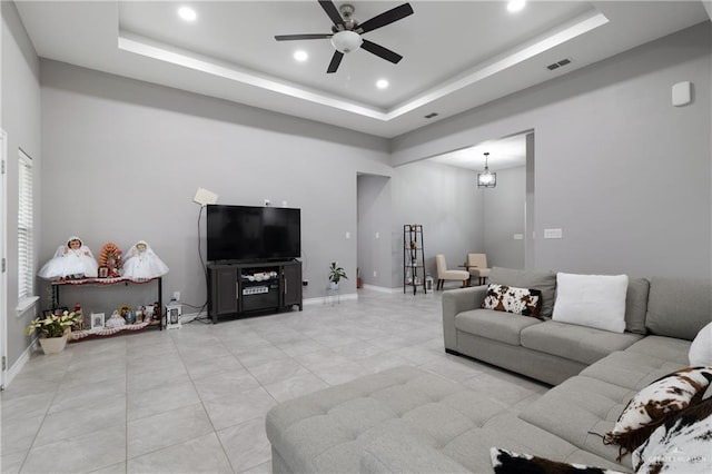 living area featuring a ceiling fan, a tray ceiling, visible vents, and baseboards