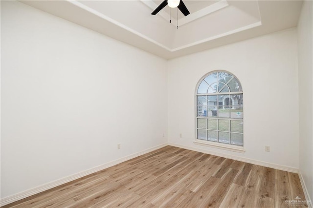 spare room featuring a tray ceiling, a ceiling fan, baseboards, and light wood finished floors