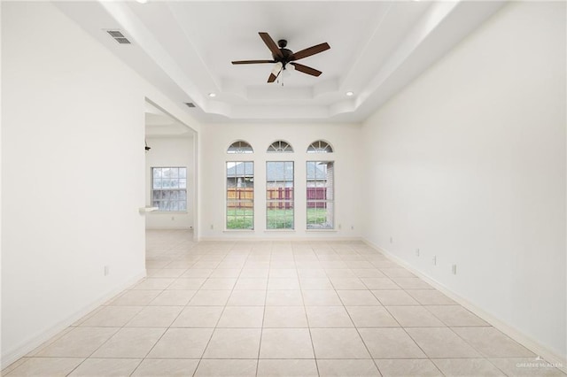 empty room with light tile patterned floors, a ceiling fan, visible vents, baseboards, and a tray ceiling