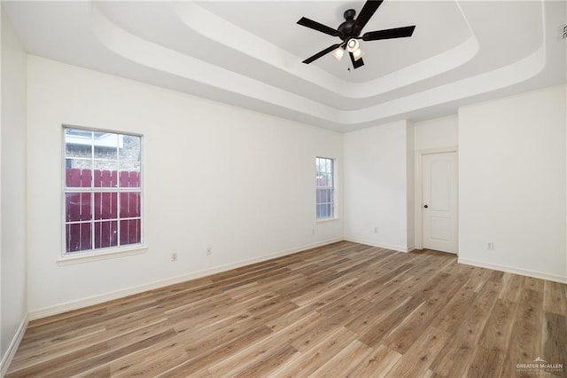 empty room with baseboards, a raised ceiling, ceiling fan, and light wood finished floors