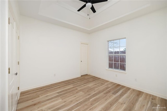 spare room with a tray ceiling, baseboards, and light wood-style floors