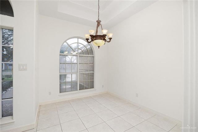 empty room featuring a raised ceiling, light tile patterned floors, baseboards, and a chandelier