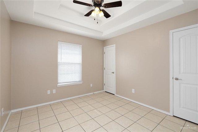 tiled spare room featuring ceiling fan and a tray ceiling