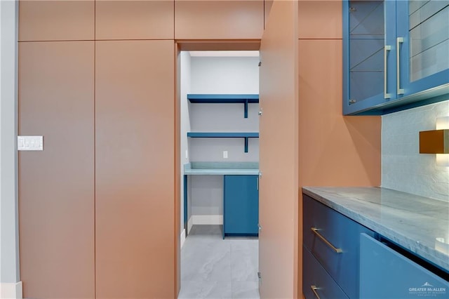 interior space with decorative backsplash, light stone counters, and blue cabinetry