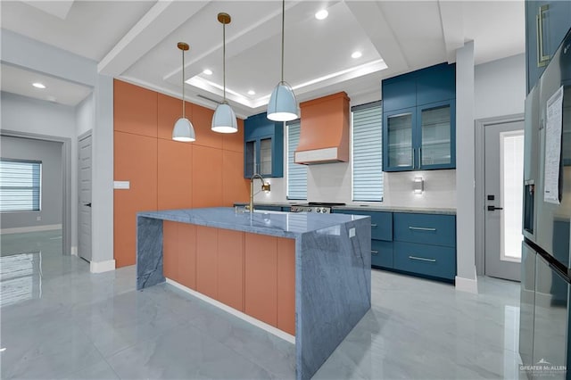 kitchen featuring a raised ceiling, premium range hood, hanging light fixtures, and an island with sink