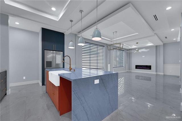 kitchen featuring a center island with sink, ceiling fan, hanging light fixtures, and a tray ceiling