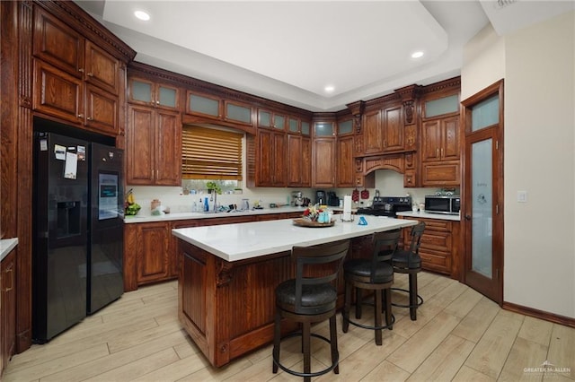 kitchen featuring black appliances, a center island, a kitchen bar, and light wood-type flooring