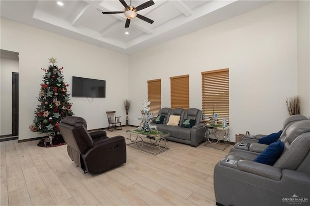 living room featuring a towering ceiling, light hardwood / wood-style flooring, ceiling fan, and coffered ceiling