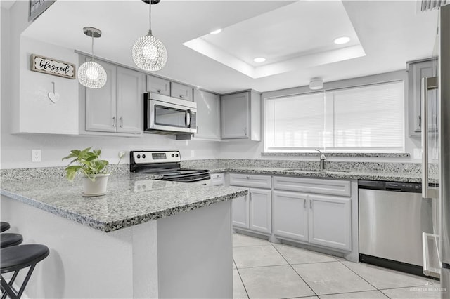 kitchen with appliances with stainless steel finishes, a raised ceiling, a peninsula, and a sink