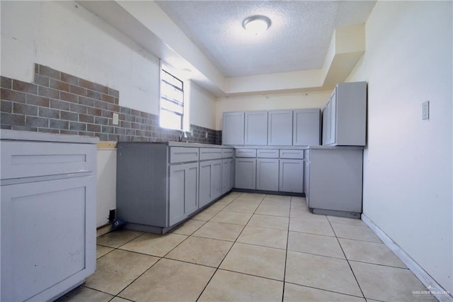 28099 Nelson Rd, San Benito, TX 78586 - kitchen with light tile patterned flooring, decorative backsplash, a textured ceiling, gray cabinetry, and a raised ceiling
