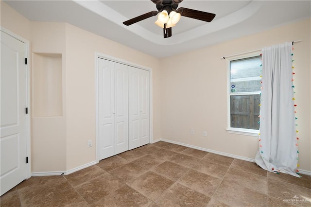 unfurnished bedroom with a raised ceiling, ceiling fan, and a closet