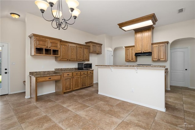 kitchen with dark stone countertops, a kitchen island with sink, decorative light fixtures, and a notable chandelier