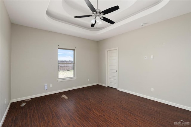 spare room with a raised ceiling, baseboards, dark wood-type flooring, and ceiling fan