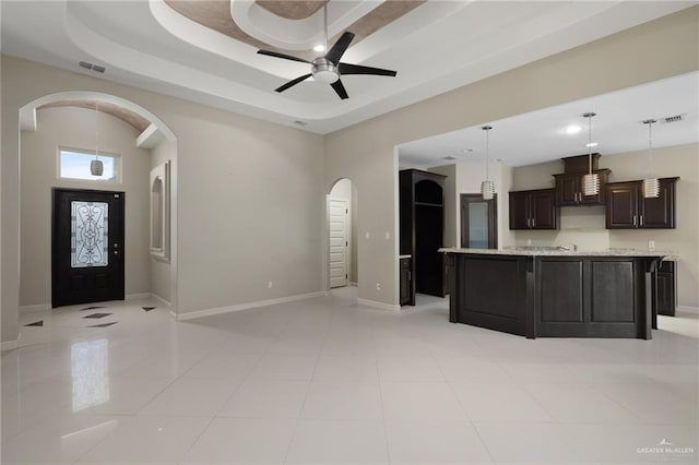 kitchen with visible vents, a tray ceiling, arched walkways, baseboards, and hanging light fixtures