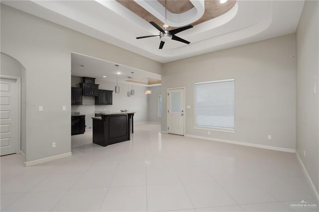 kitchen featuring a tray ceiling, arched walkways, ceiling fan, light countertops, and open floor plan