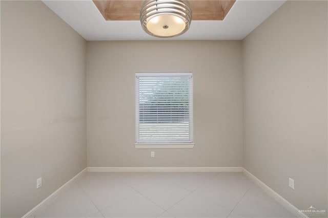 empty room featuring a raised ceiling, light tile patterned floors, and baseboards